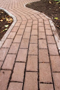 Yakın zamanda kırmızımsı dikdörtgen asfalt levhalarla döşenmiş, köşeli bir yol (virajlı) ve kaldırımlı bir platform. Her iki tarafta da düşen sonbahar yapraklarıyla kara toprak var..