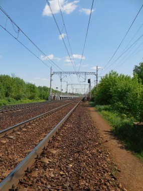 Barajdaki demiryolu, kırsal kesimde. Demiryolu, çakıl dolumu, elektrik hattı, orman kemeri ve uzakta bir tren istasyonu..