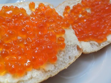 Lezzetli, lezzetli kırmızı havyar beyaz ekmek üzerine tereyağlı, beyaz tabakta.