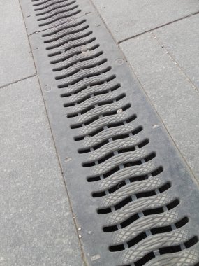 Sokaktaki drenaj tepsisinin metal ızgarası (fırtına kanalizasyonu) gri asfalt levhalarla kaplıdır..