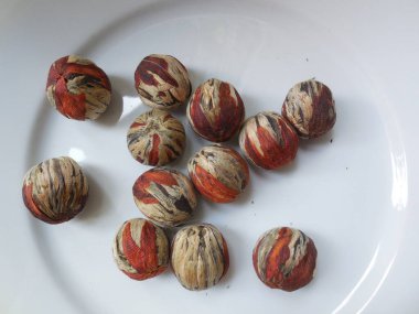 Beyaz bir tabağın arka planında, yoğun, pürüzsüz, çok renkli toplar şeklinde seçkin, pahalı yeşil çay. İçtikten sonra, toplar güzel bir kasımpatı çiçeği şeklinde çiçek açar..