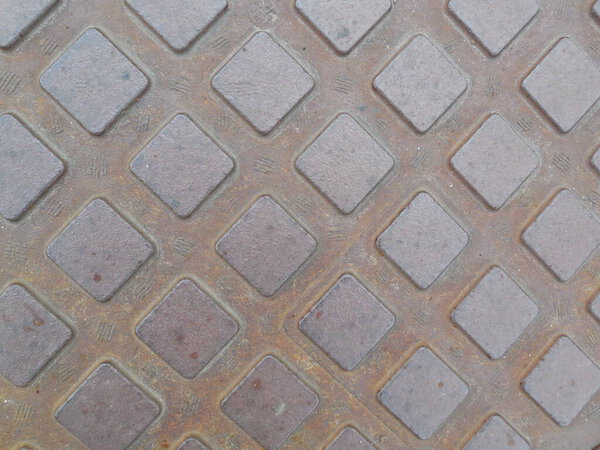 A relief pattern of identical squares on the rusty metal surface of the hatch cover. Photo without highlighting the focal object.