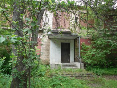 Metal ve tahtalarla kaplı, ağaçlarla kaplı, iki katlı terk edilmiş tuğla bir bina..