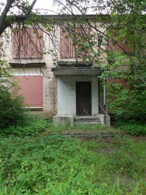 Metal ve tahtalarla kaplı, ağaçlarla kaplı, iki katlı terk edilmiş tuğla bir bina..