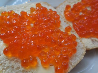 Lezzetli, lezzetli kırmızı havyar beyaz ekmek üzerine tereyağlı, beyaz tabakta.