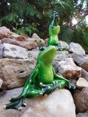 Komik kurbağalar (sevimli yeşil figürler, hatıra oyuncakları) bahçede güzel taşlar üzerinde ve yoga yaparlar..