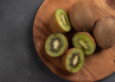 Mutfak masasındaki ahşap tabakta dilimlenmiş taze kivi meyvesi ve bütün kivi meyvesi. Masadaki kiviyi kapat.