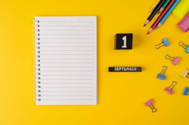 Not defteri ve ahşap takvim. 1 Eylül 'de okul malzemeleriyle sarı arka planda, düz manzaralı.