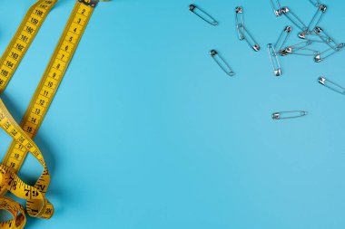 İğneler ve mezura ölçer, santimetre şeklinde göstergeler. Yuvarlak santimetre cetvel, sarı ve metal raptiyeler. El işi ve dikiş konsepti. Boşluğu kopyala