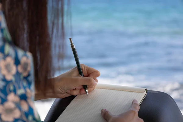 Unrecognisable woman writing looking out to sea — Stock Photo, Image