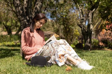 Kadın bahçede oturmuş kitap okuyor.