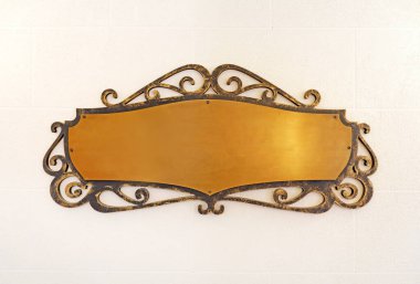 Eski pirinç, sarı, metal bir plaka çerçevelenmiş ve duvara çivilenmiş.