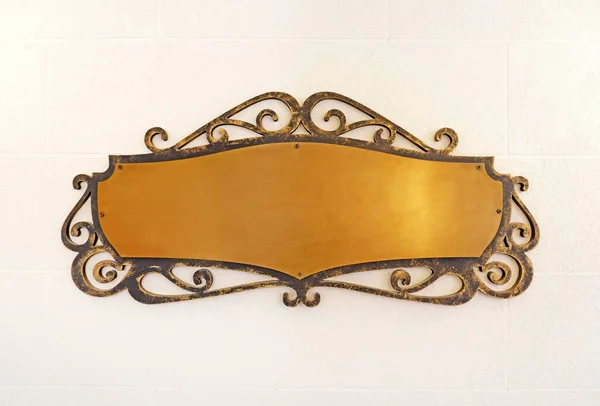 Eski pirinç, sarı, metal bir plaka çerçevelenmiş ve duvara çivilenmiş.