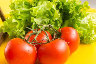 Yeşil dallı kırmızı domatesler, büyük soluk benizli. Arka planda marul yaprakları. Pişirmek için sebzeler.