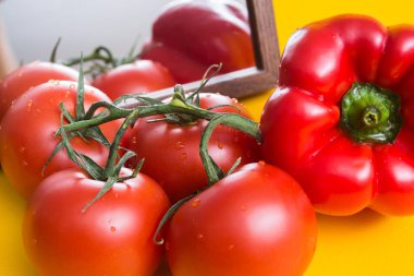 Aynanın yanındaki sarı masada kırmızı olgun domatesler. Mutfağa sebze ve yiyecek seriyorum. Kırmızı biber yansıtılır
