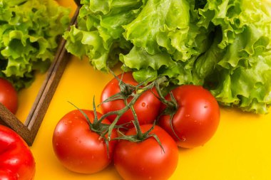 Yeşil dallı kırmızı domatesler, büyük soluk benizli. Arka planda marul yaprakları. Pişirmek için sebzeler.