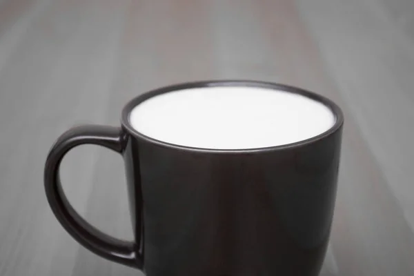 Taza negra con leche blanca sobre la mesa. Desayuno ligero en casa. — Foto de Stock