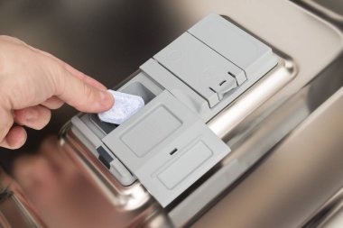 Bir el bulaşık makinesi tabletini deterjan tepsisine koyar..