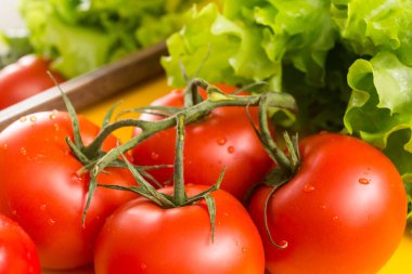 Yeşil dallı kırmızı domatesler, büyük soluk benizli. Arka planda marul yaprakları. Pişirmek için sebzeler.