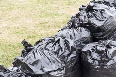 Yeşil çimenlikte çöp standı dolu siyah torbalar..