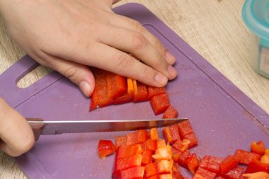 Tahtada kırmızı biber dilimliyorum. Eller dolmalık biberi küp küp doğradı. Ev mutfağında yemek yapmak..