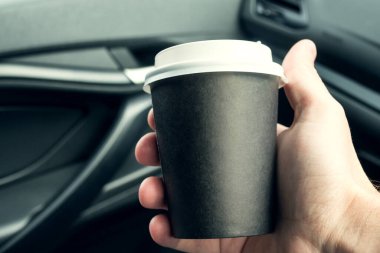 Bir adam elinde bir fincan kahve tutuyor. Arabanın içinde. Yoldan çekilin. Sabah kahvesi.
