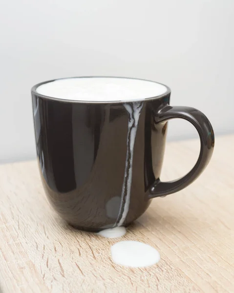 Du lait dans une tasse noire. Gouttes sur la table. — Photo