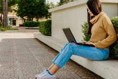 Chica estudiando con laptop on plaza al aire libre sonrriendo