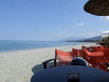 Yunan plajı, deniz kenarında dağ ve kumsalda bir masa.