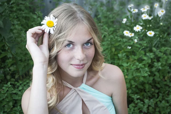 Young beautiful girl with long blond curvy hair among bushes with flowers.