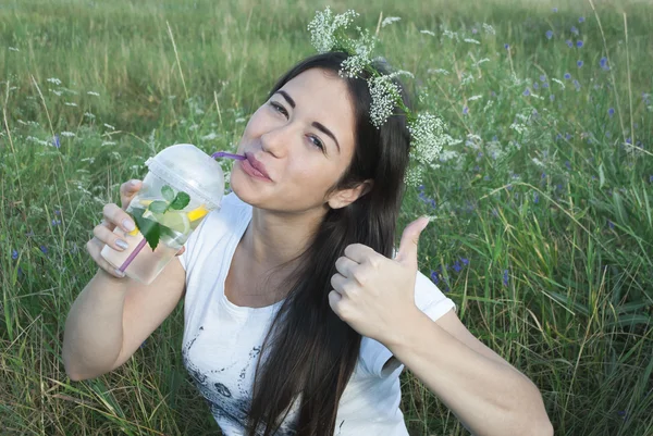 Bella giovane donna sullo sfondo della natura, bere acqua con limone e menta — Foto Stock