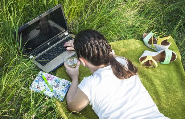 Kız bir dizüstü bilgisayar ve bir dizüstü bilgisayar ile çim üzerinde yalan