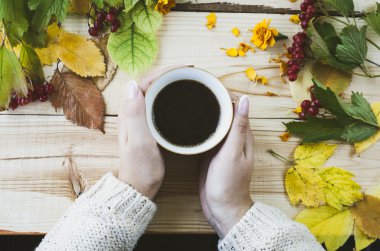Kadınların elleri ile bir fincan kahve sonbahar arka plan üzerinde bırakır