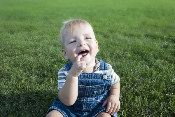 Маленький мальчик сидит на траве в солнечный день — стоковое фото