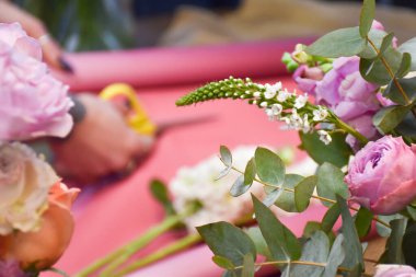 Çiçekçi gül buketi yapmak için pembe kağıt kesiyor.