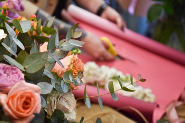 Çiçekçi gül buketi yapmak için pembe kağıt kesiyor.