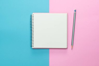 Pastel mavisi pembe arka planda eskiz defteri ve kalem. Üst manzara, düz uzanma