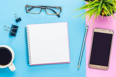 Kahve fincanı, akıllı telefon, gözlük, not defteri olan ofis masasının üst görüntüsü