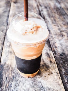 Buzlu kahve ve pipet kahverengiydi. Ahşap masanın üzerinde plastik bardakta krema vardı.