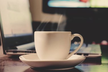 Ahşap masada dizüstü bilgisayarı olan fincan kahve.