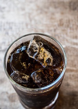 Ahşap masanın üstünde buzla kaplı bir bardak kola.