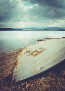 Bulutlu bir günde, Polonya 'da bir göl kıyısında, dağ manzarasına karşı eski bir yelkenli.