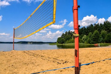 Plaj voleybol sahası güneşli bir günde göl ve ormanın yanında yer alır.