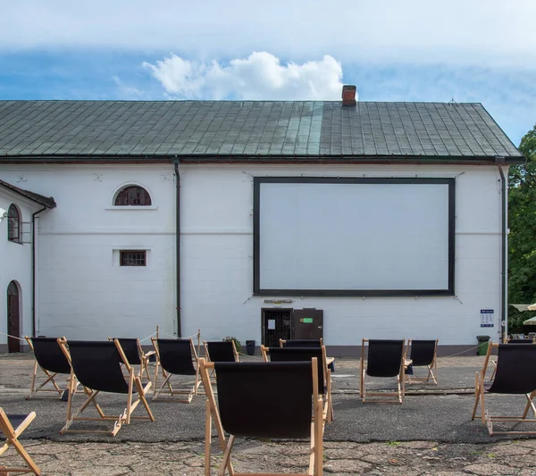 Oper-air, outdoor cinema in the yard of brewery in Zwierzyniec, Poland. Rows of simple, black sunbeds in front of screen installed on the wall.