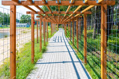 Göl ayakkabısı ve orman boyunca uzanan kaldırımın üzerindeki ahşap pergola (treillage). Tek noktalı perspektif.