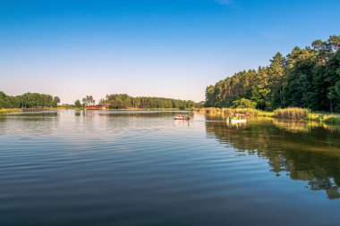 Akşam ışığında güzel bir göl manzarası. Pedallı teknelerde yüzen insanlar. Orman ve arka planda ahşap bir iskele. Krasnobrod, Roztocze, Polonya. 