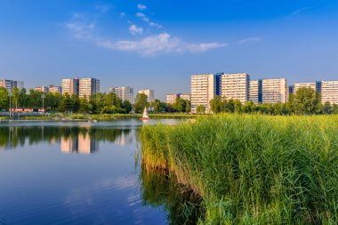 View at Tysiaclecie district in Katowice on a beautiful, sunny day, seen through the pond. Apartment buildings situated neat the lake against blue sky.  clipart