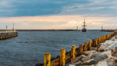 Baltık Denizi 'ndeki Darlowo limanına giren bir yolcu gemisi, arka planda trafik ışıkları, beton iskele manzarası.