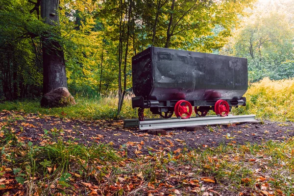 A restored mine cart displayed in the park in Katowice as a symbol of the mining tradition. Black box of a wagon on red wheels placed on a fragment of a railway track.