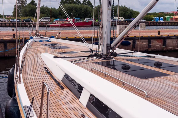 Wooden deck of a large yacht moored in the port of Darlowo, Poland, on the Baltic Sea. Bushes and cars parked on the other side of the harbor canal.